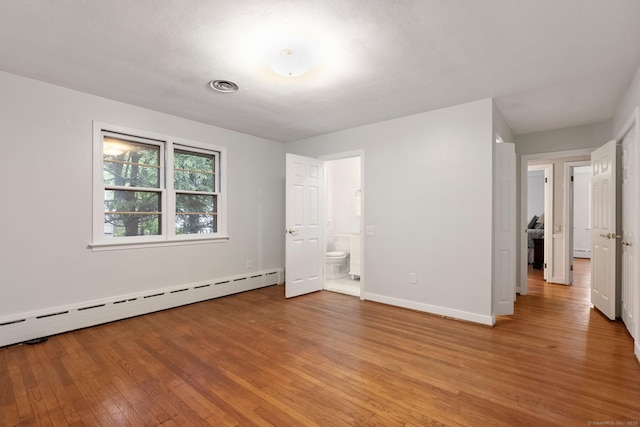 unfurnished bedroom featuring a baseboard radiator, light wood-style flooring, baseboards, and connected bathroom