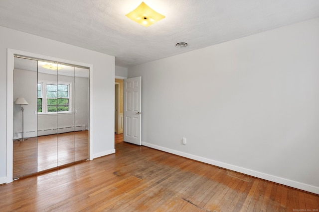 unfurnished bedroom featuring baseboard heating, baseboards, light wood-style flooring, and a closet