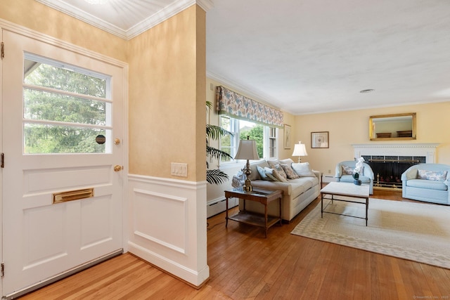 entryway featuring crown molding, light wood-type flooring, a baseboard radiator, a fireplace, and a wainscoted wall
