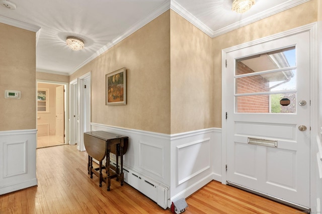 doorway to outside featuring wainscoting, light wood-type flooring, crown molding, a decorative wall, and baseboard heating