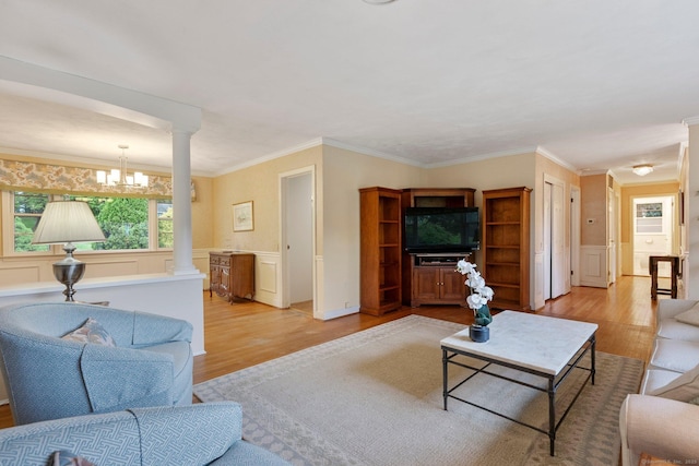 living room featuring light wood-style flooring, ornate columns, crown molding, a chandelier, and a wainscoted wall