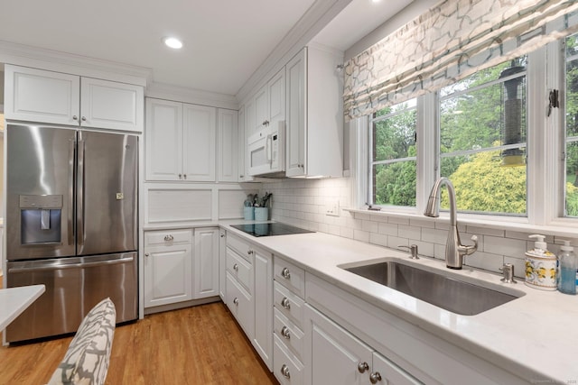 kitchen with stainless steel fridge, a sink, white microwave, light countertops, and white cabinetry