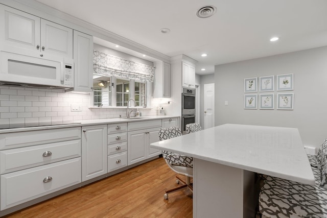 kitchen with white microwave, a sink, decorative backsplash, light wood-style flooring, and recessed lighting