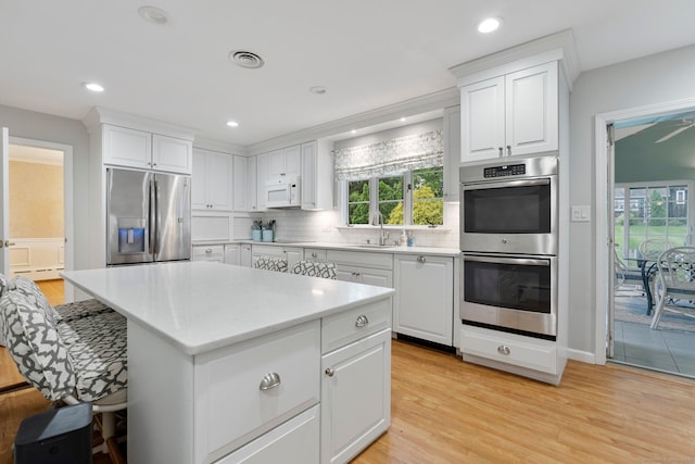 kitchen with appliances with stainless steel finishes, a sink, decorative backsplash, light countertops, and healthy amount of natural light