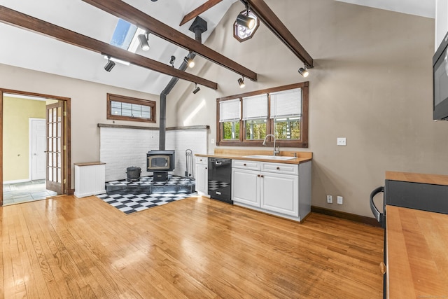 kitchen with a sink, track lighting, black appliances, light wood-style flooring, and a wood stove
