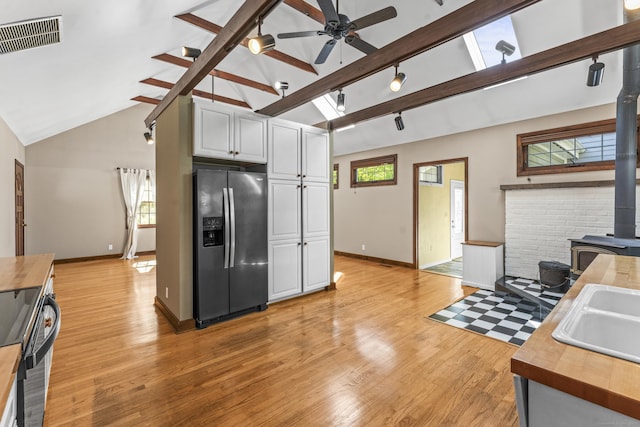 kitchen featuring stainless steel fridge with ice dispenser, butcher block countertops, a wood stove, baseboards, and range with electric cooktop