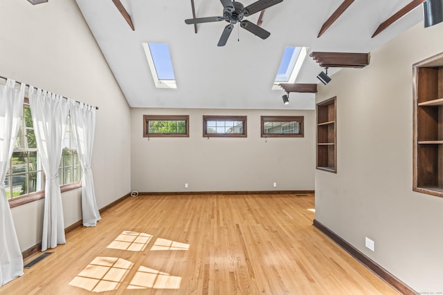 spare room with a skylight, ceiling fan, light wood-type flooring, and baseboards
