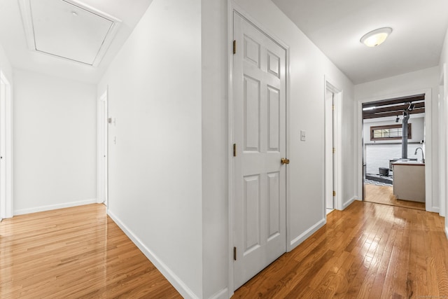 hallway featuring light wood finished floors, attic access, and baseboards