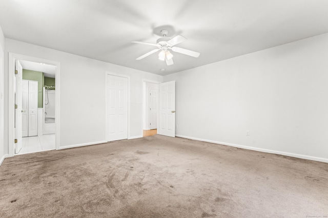 unfurnished bedroom featuring carpet, baseboards, ensuite bath, and a ceiling fan