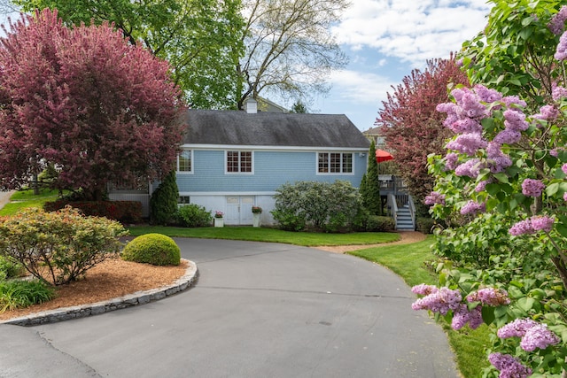 view of front of home featuring curved driveway, stairs, a front yard, and a shingled roof