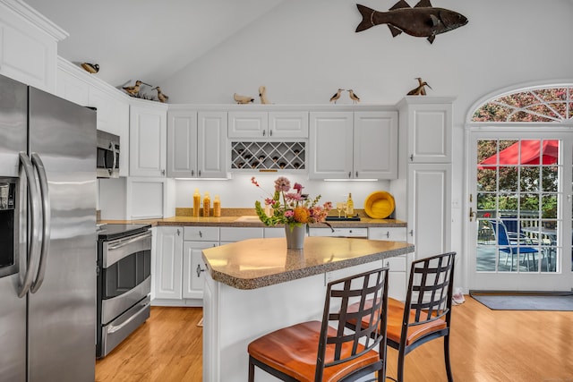 kitchen featuring appliances with stainless steel finishes, a kitchen bar, white cabinets, light wood finished floors, and high vaulted ceiling