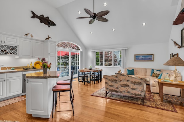 kitchen featuring high vaulted ceiling, a breakfast bar area, white cabinetry, a kitchen island, and light wood finished floors