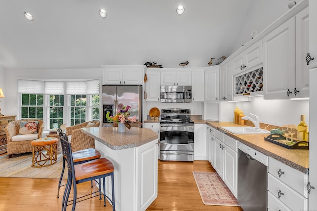 kitchen featuring stainless steel appliances, a sink, white cabinets, a center island, and recessed lighting
