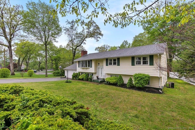 bi-level home with a garage, a chimney, a front yard, and central AC