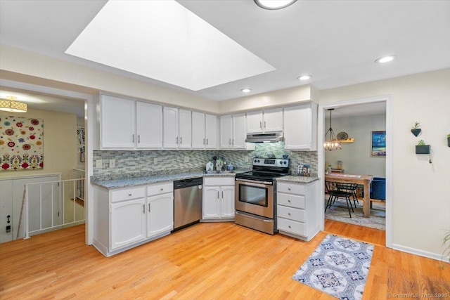kitchen with under cabinet range hood, light wood finished floors, backsplash, white cabinets, and appliances with stainless steel finishes