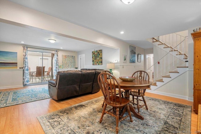 dining space with light wood-style flooring, stairs, a decorative wall, and a wainscoted wall