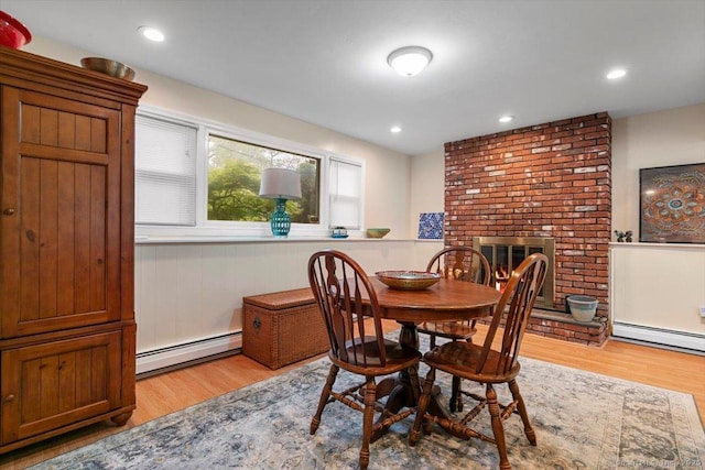 dining space with light wood-type flooring, baseboard heating, and a brick fireplace