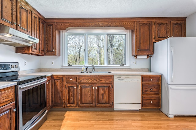 kitchen with white appliances, under cabinet range hood, a sink, light countertops, and a textured ceiling