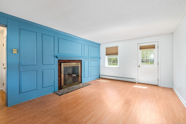 unfurnished living room with baseboard heating, light wood-type flooring, a fireplace, a textured ceiling, and baseboards