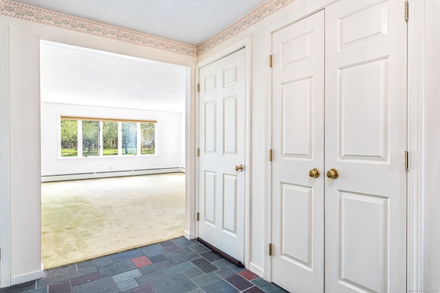 hallway with a baseboard radiator, dark colored carpet, a textured ceiling, and dark stone finish flooring