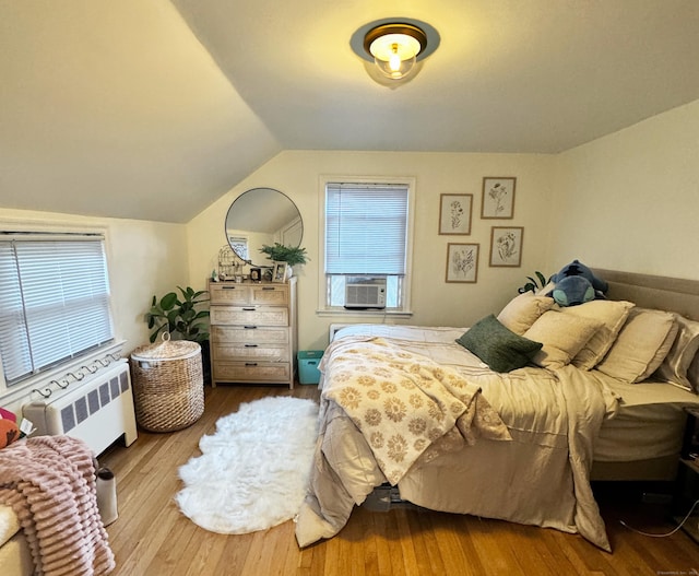 bedroom featuring radiator, wood finished floors, vaulted ceiling, and cooling unit