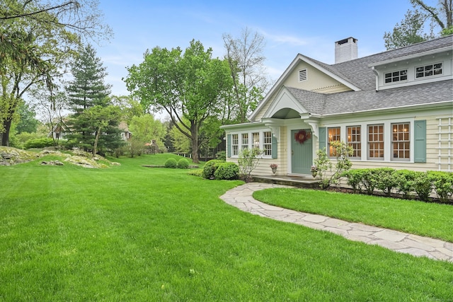 view of front of property featuring a shingled roof, a front lawn, and a chimney