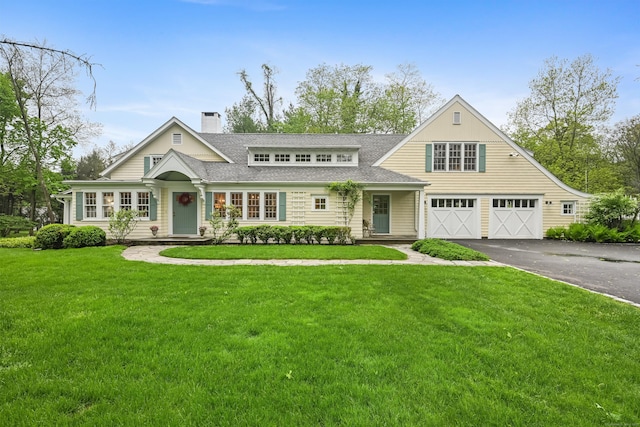 shingle-style home featuring asphalt driveway, a garage, a chimney, a front yard, and a shingled roof
