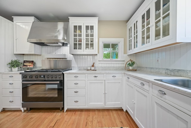 kitchen with exhaust hood, gas stove, light wood-style flooring, white cabinets, and glass insert cabinets