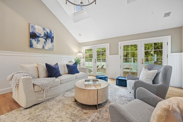 living area with french doors, wainscoting, wood finished floors, a skylight, and lofted ceiling