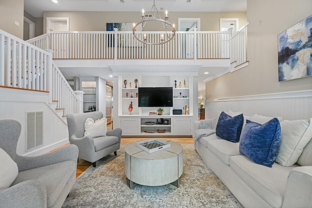 living room with wainscoting, stairs, a chandelier, a high ceiling, and wood finished floors