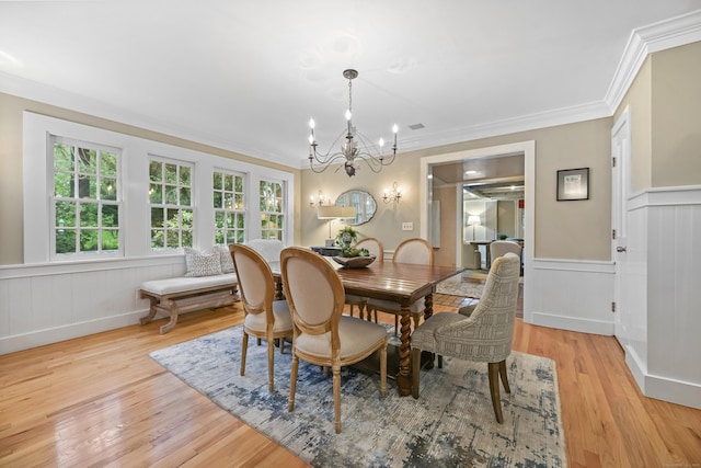 dining room with a chandelier, light wood-style flooring, crown molding, a wainscoted wall, and a decorative wall