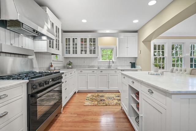 kitchen featuring gas stove, extractor fan, a sink, light wood-type flooring, and white cabinets