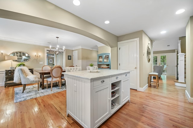 kitchen with light wood-style flooring, a center island, hanging light fixtures, arched walkways, and a chandelier