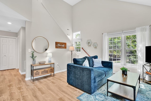 living room featuring a high ceiling, light wood-style flooring, baseboards, and stairway