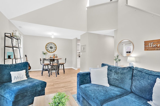 living area featuring light wood-style floors, baseboards, and a towering ceiling