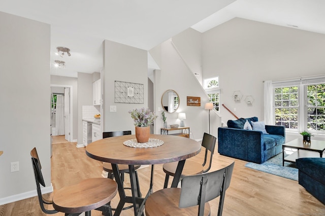 dining space featuring plenty of natural light, light wood-style floors, wine cooler, high vaulted ceiling, and baseboards