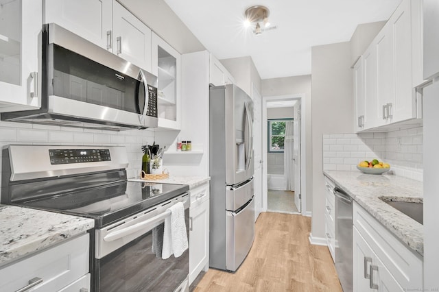 kitchen with appliances with stainless steel finishes, white cabinetry, light wood-type flooring, and decorative backsplash