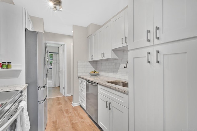 kitchen featuring appliances with stainless steel finishes, a sink, light wood-type flooring, white cabinets, and tasteful backsplash