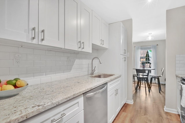 kitchen with a sink, stainless steel appliances, white cabinetry, light wood finished floors, and tasteful backsplash