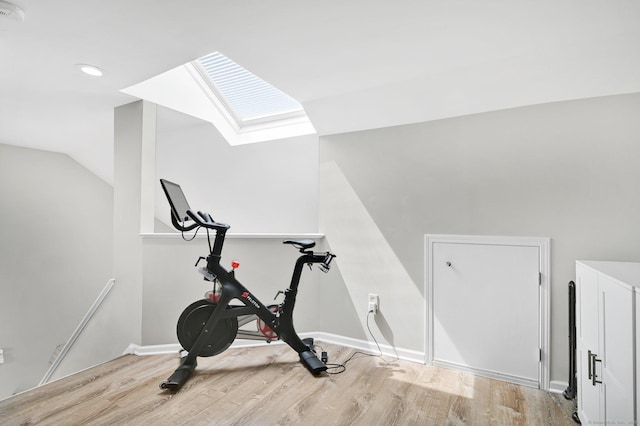 workout room featuring wood finished floors, a skylight, lofted ceiling, and baseboards
