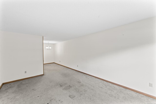 spare room featuring a chandelier, carpet flooring, and baseboards