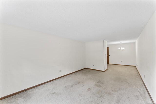 carpeted empty room featuring a chandelier and baseboards