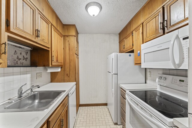kitchen with white appliances, a sink, light countertops, baseboards, and backsplash
