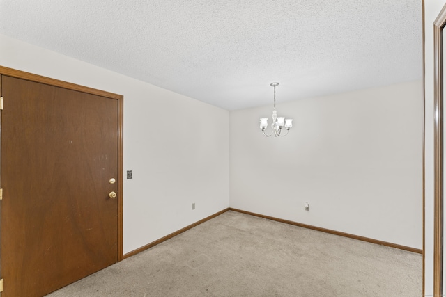 carpeted empty room featuring a chandelier, a textured ceiling, and baseboards