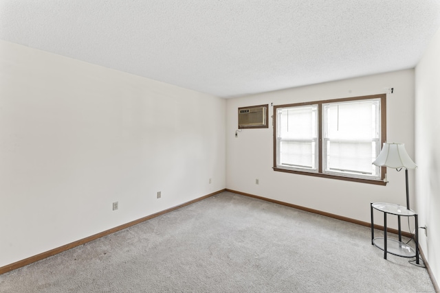 carpeted empty room featuring a textured ceiling, a wall mounted air conditioner, and baseboards