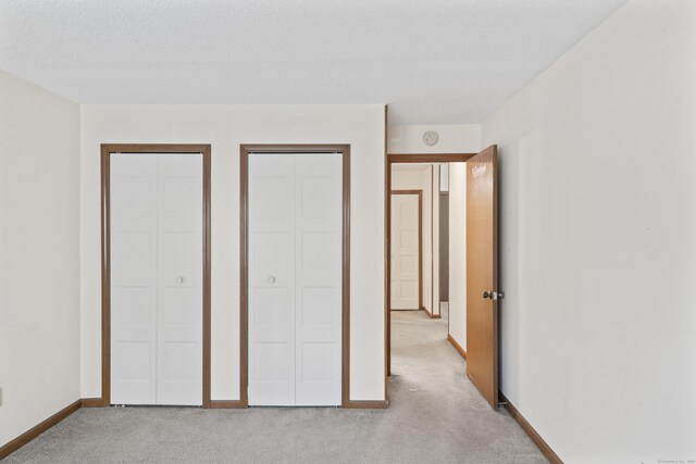 unfurnished bedroom with multiple closets, light colored carpet, baseboards, and a textured ceiling