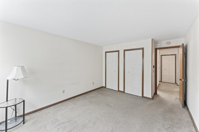 unfurnished bedroom featuring carpet, baseboards, and two closets