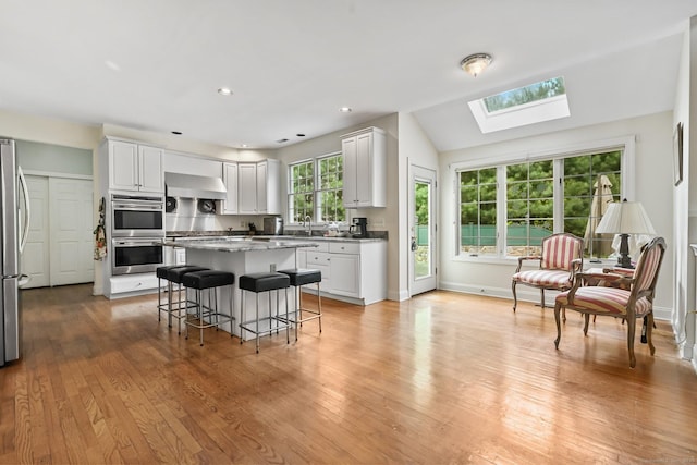 260 Range Rd, Fairfield, CT 06890 - kitchen with stainless steel appliances, wall chimney range hood, a breakfast bar area, white cabinets, and a center island