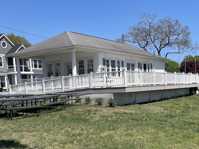 rear view of property featuring a yard, a deck, and a shingled roof