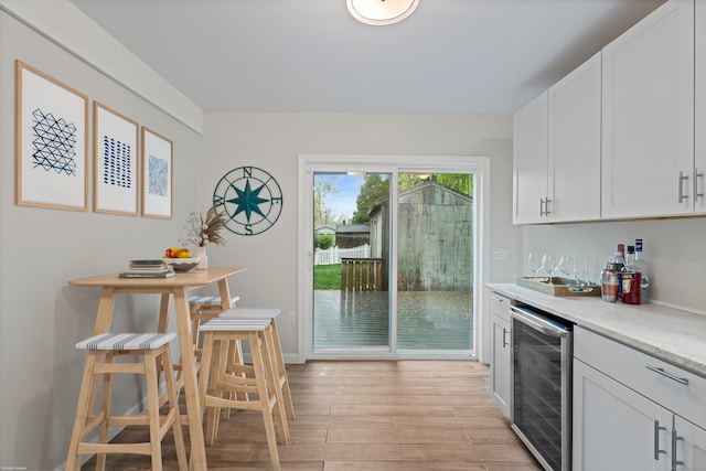 kitchen featuring beverage cooler, light wood-style flooring, white cabinetry, light stone countertops, and baseboards